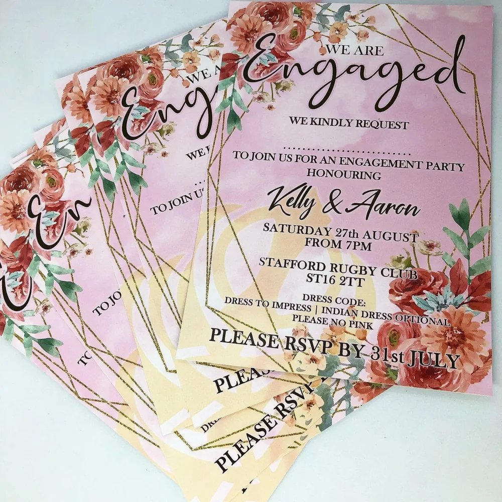 Pink floral engagement invitations arranged in an overlapping stack