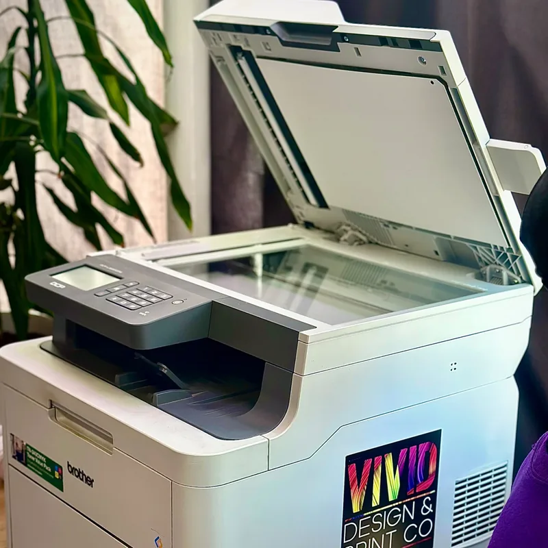 Brother photocopier with its scanner lid open and Vivid Design & Print Co branding.