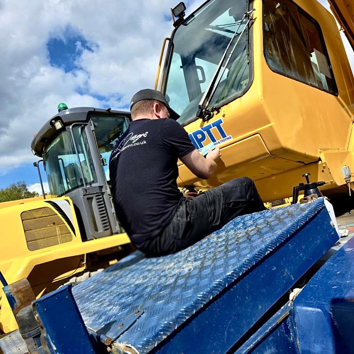 Vivid Design & Print Co applying printed graphics to a yellow excavator in Stafford